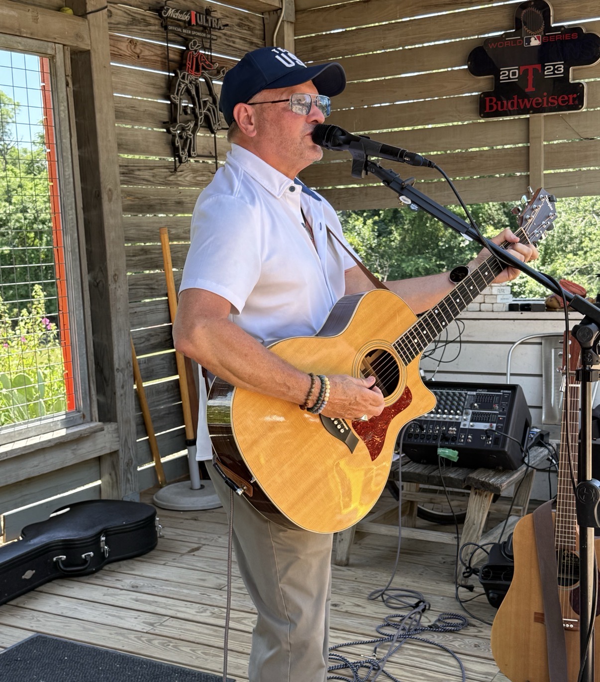 John Geyerman singing into a microphone and playing acoustic guitar on a covered patio